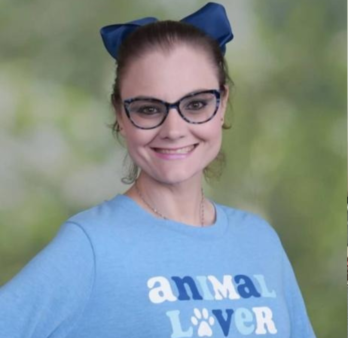 A white woman with a big blue bow in her hair, glasses, and a blue animal lover shirt